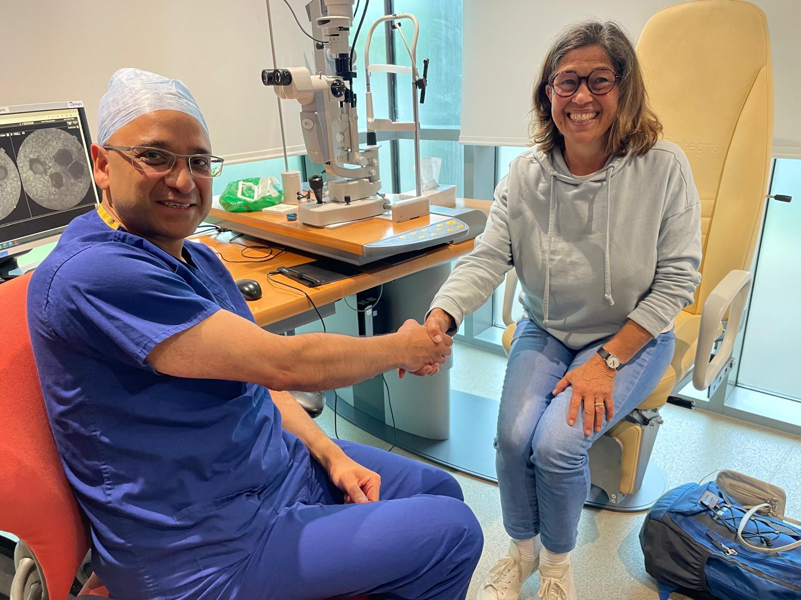Angela Young, a white female in her early 60s in eye clinic shaking hands with consultant ophthalmologist. Both smiling and looking to camera 