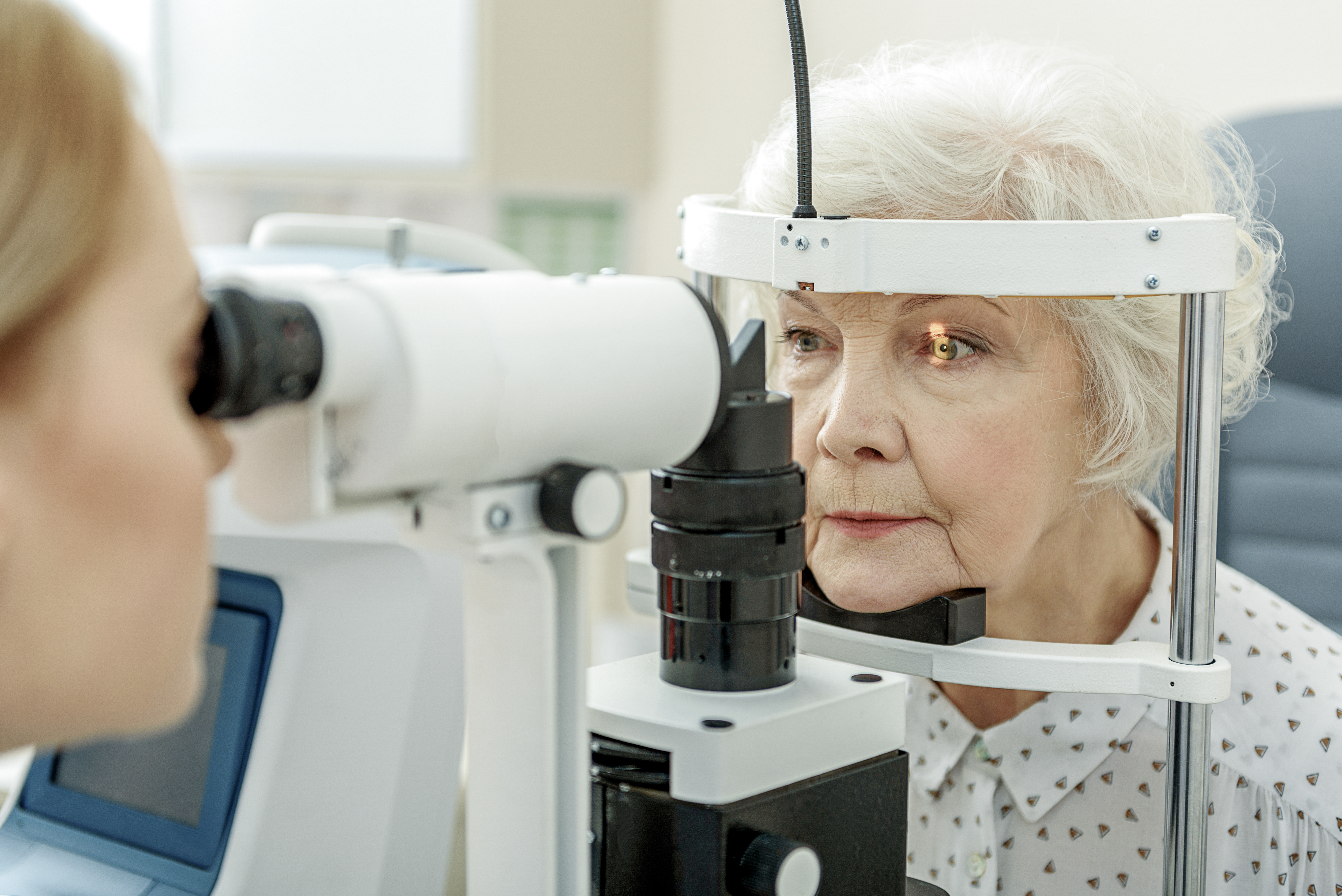 Elderly woman leaning into eye examination machine.