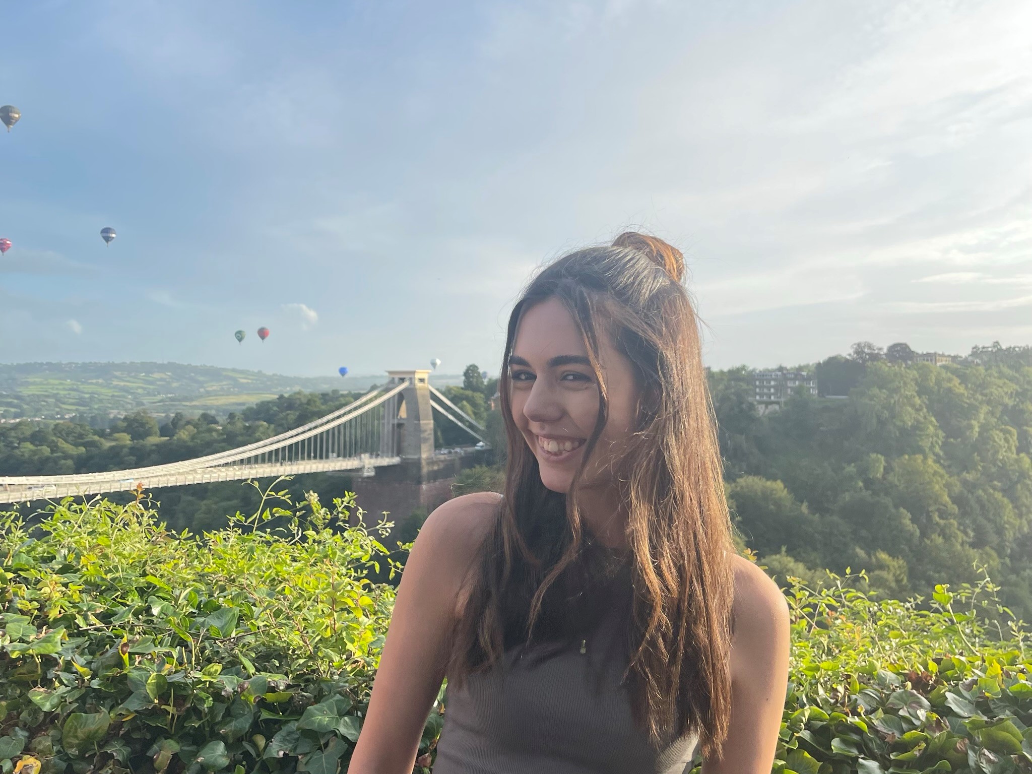 Emily, a white female in her 20s with long dark hair, smiling and posing with the Clifton Suspension Bridge in the background