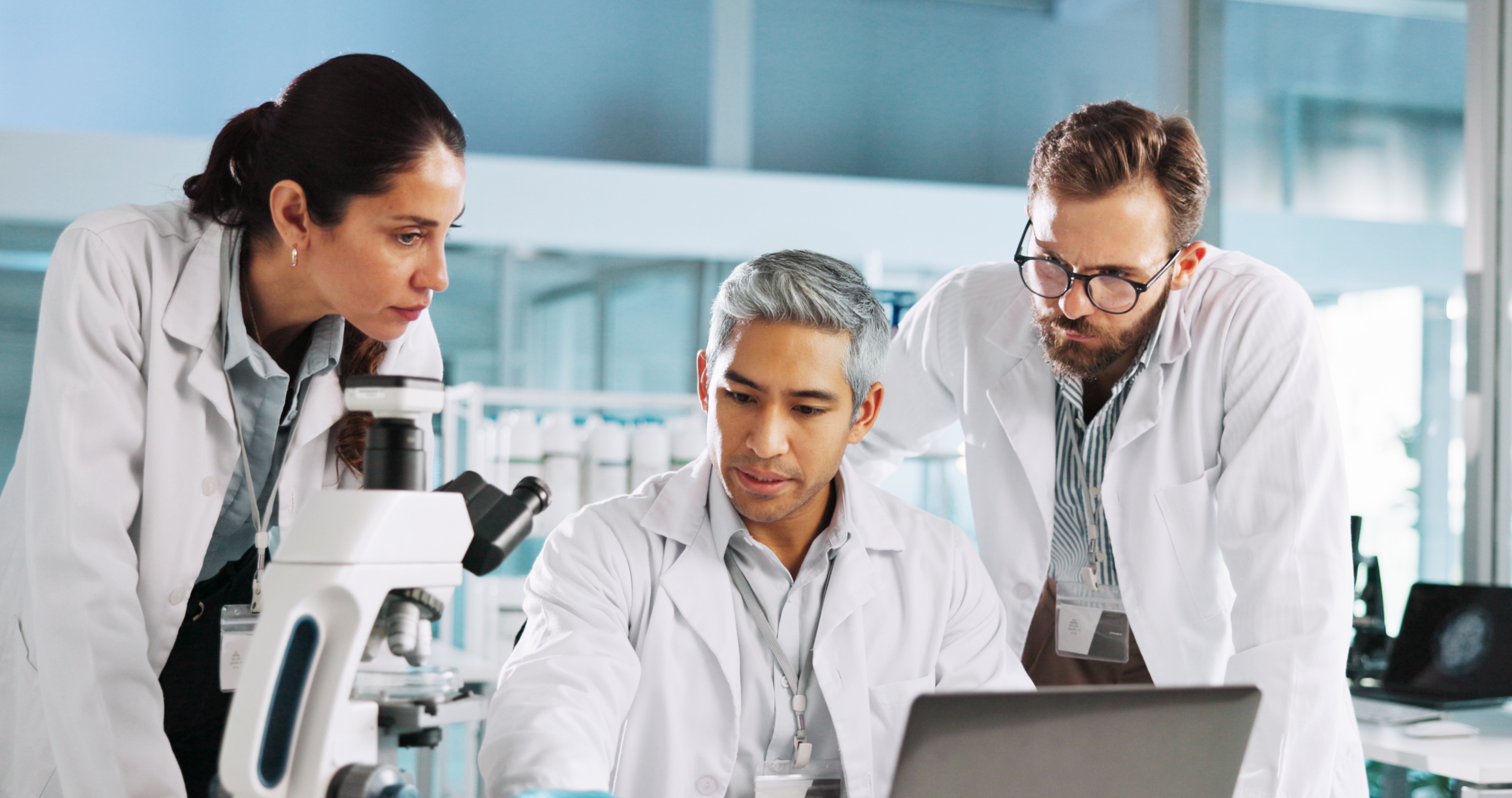 Three researchers with a microscope and laptop in the laboratory