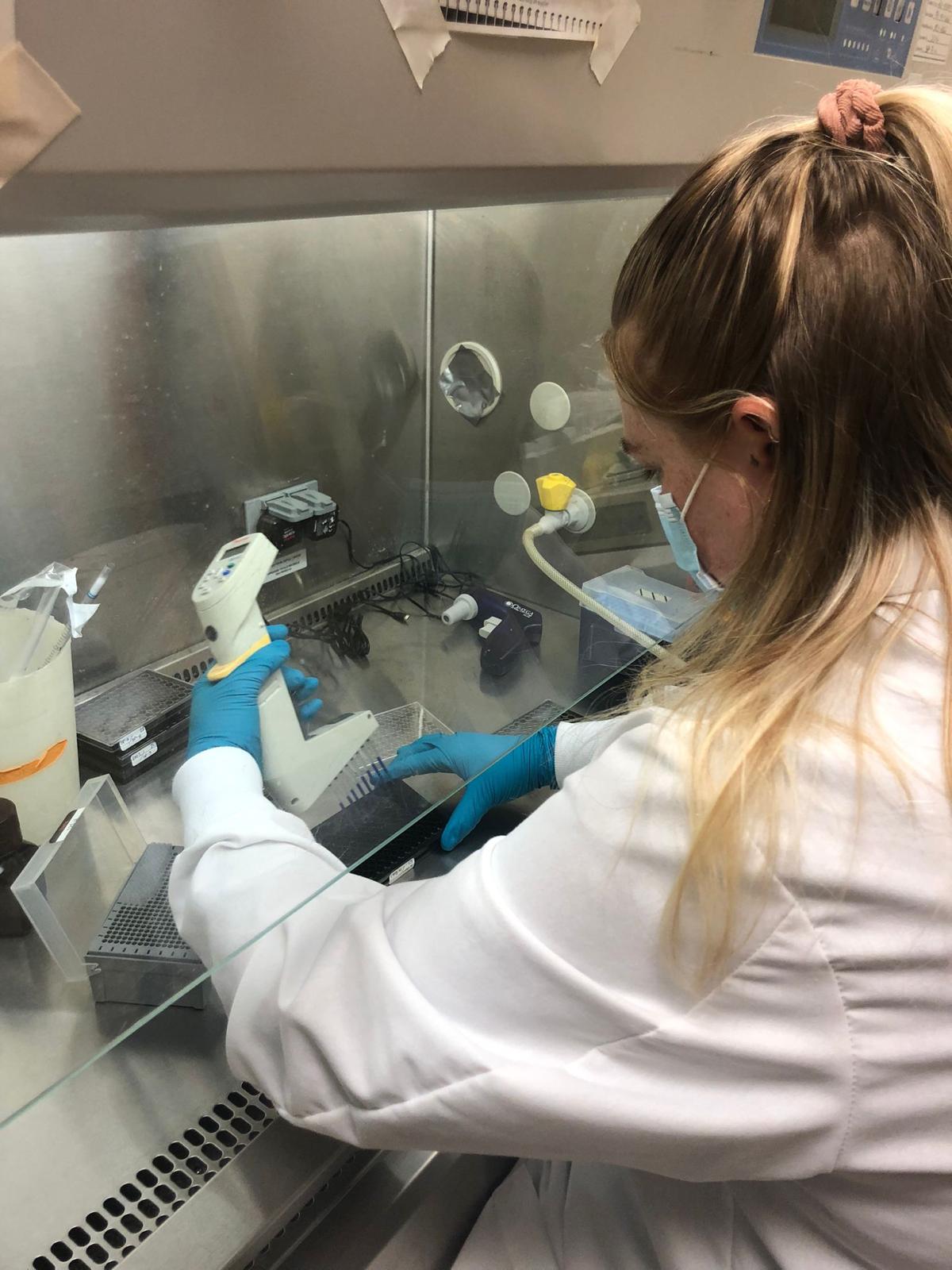 Elisha Griffin in the lab wearing a white lab coat, a face mask, and blue gloves, holding a scanner for an experiment