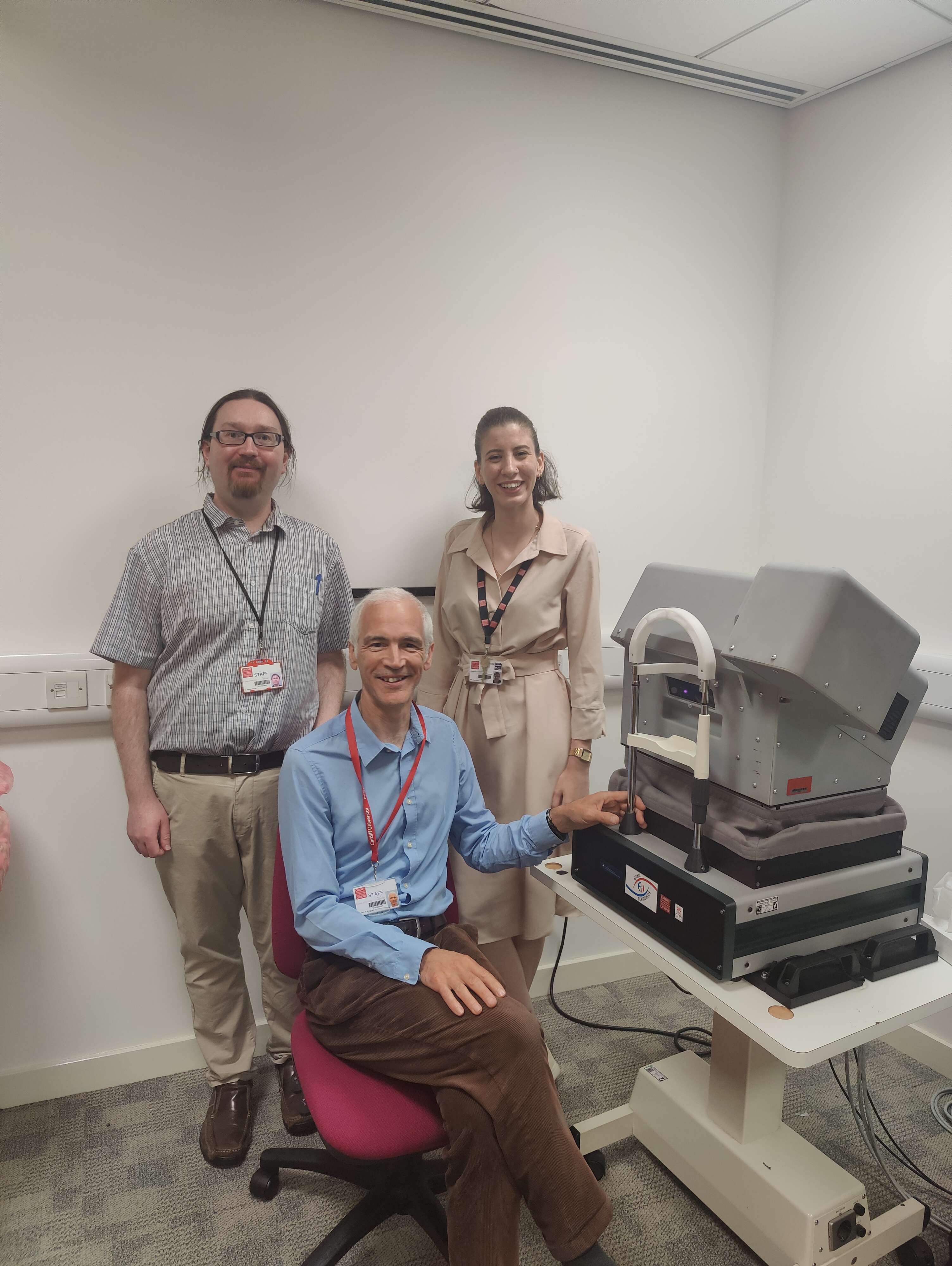 Image of the Cardiff research team, stood next to optometry equipment, a large eye scanner. 
