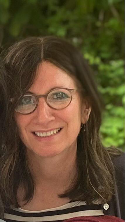 Elena Schiff. A white woman with long dark hair and glasses. She is smiling. 