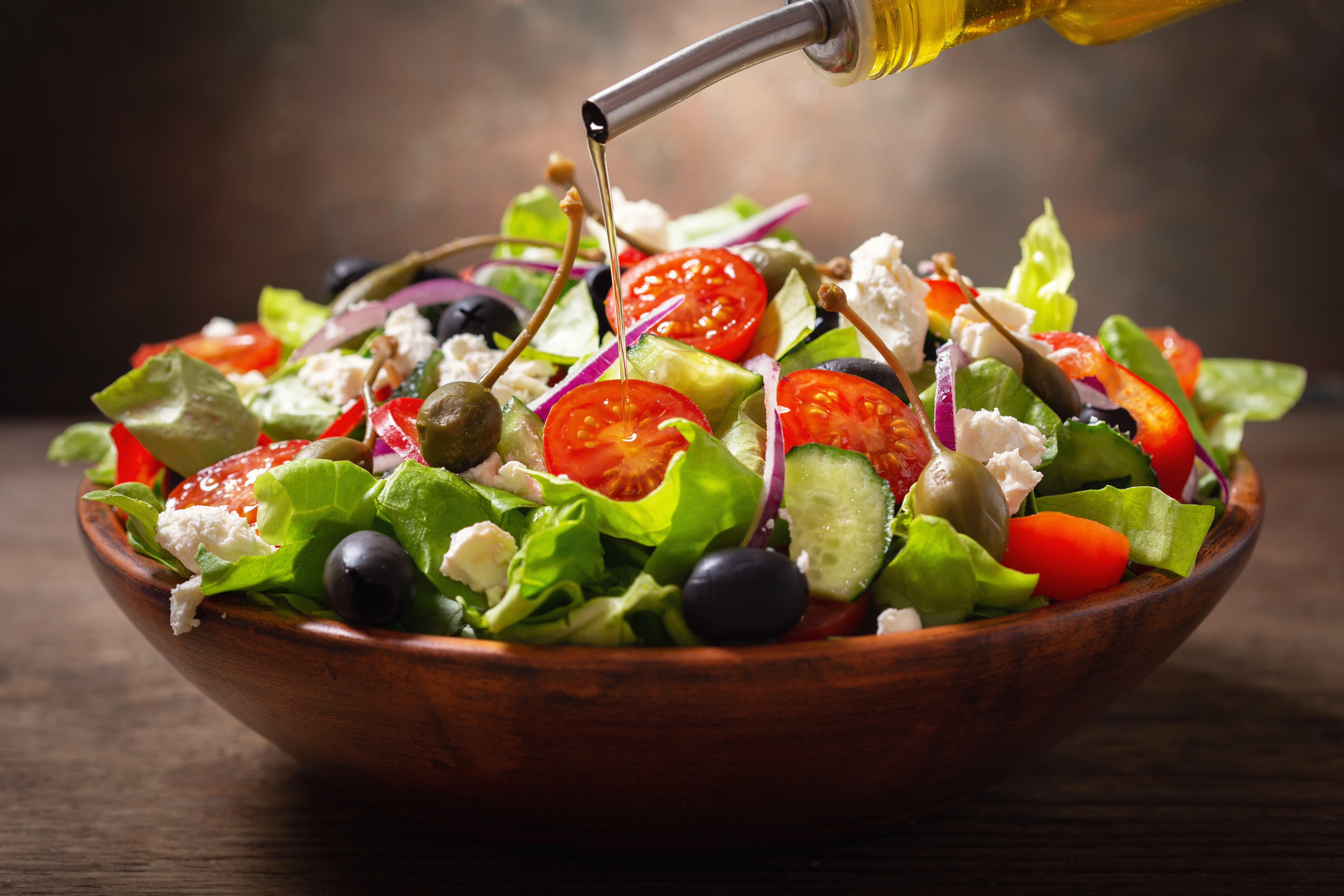 summer Greek salad in a bowl being drizzled with olive oil