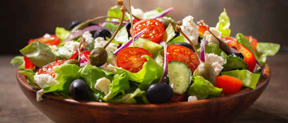summer Greek salad in a bowl being drizzled with olive oil