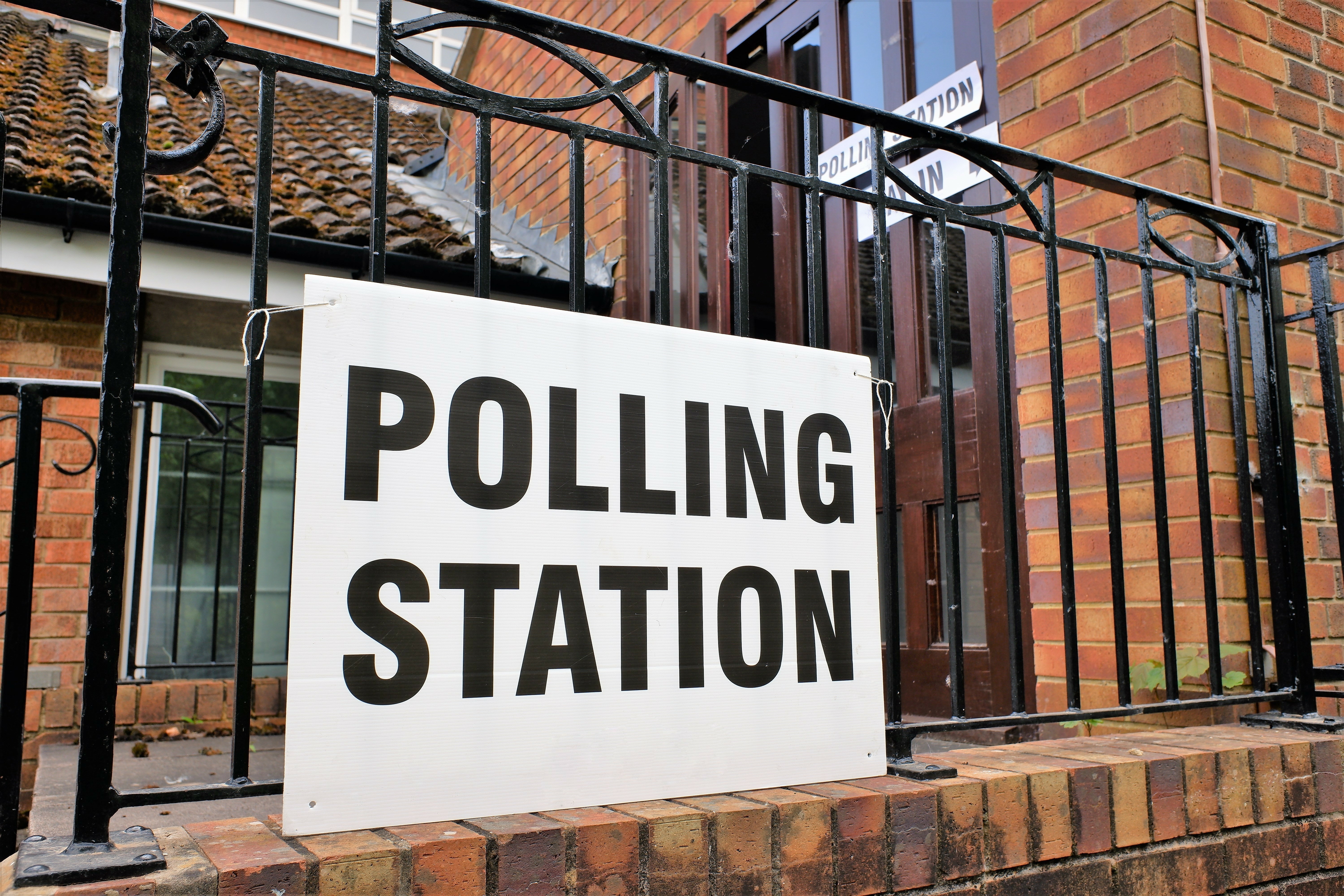 Polling station sign hanging on a black railing with a brick building in the background