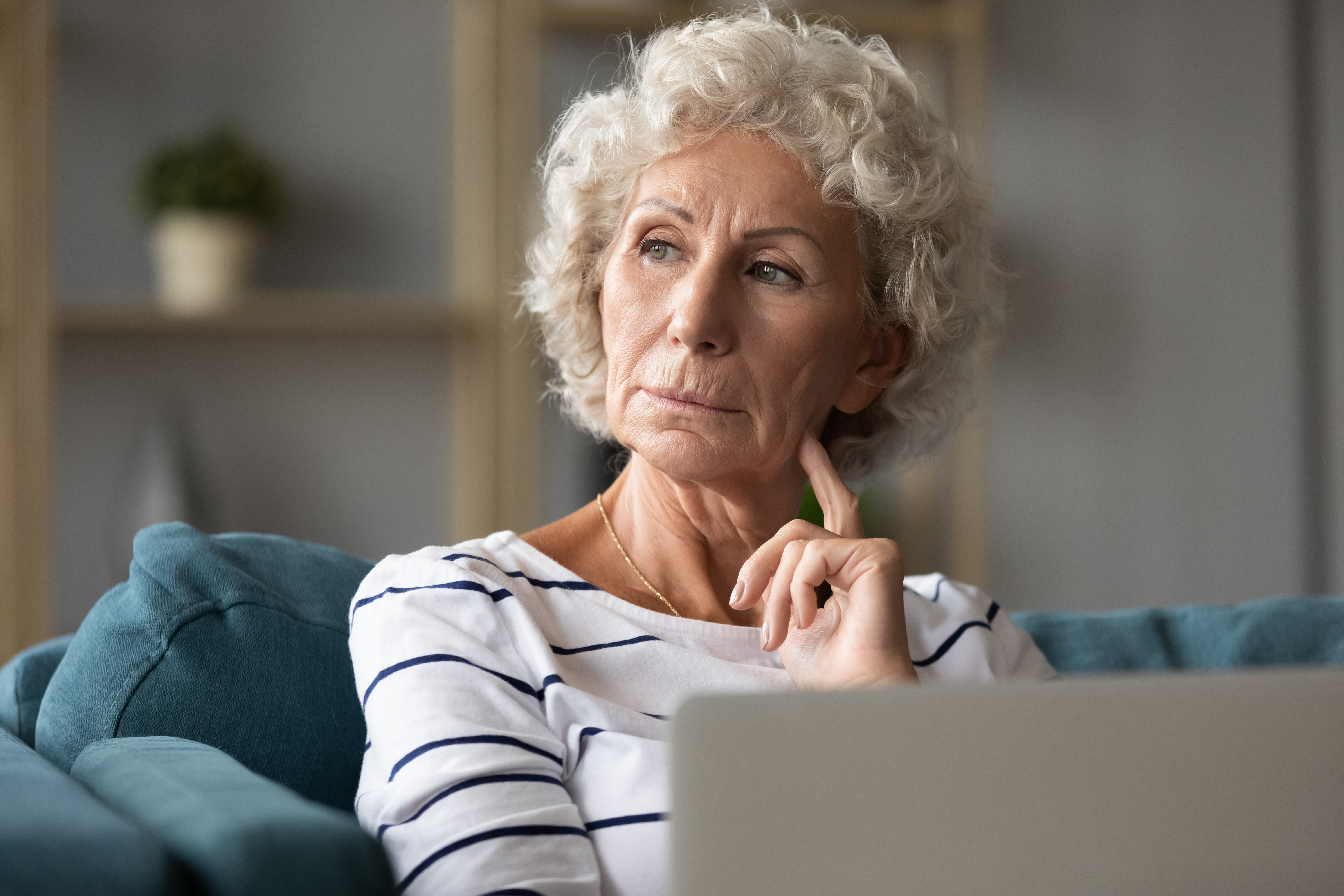 Aged Woman Sitting On Sofa With Laptop Looking Away