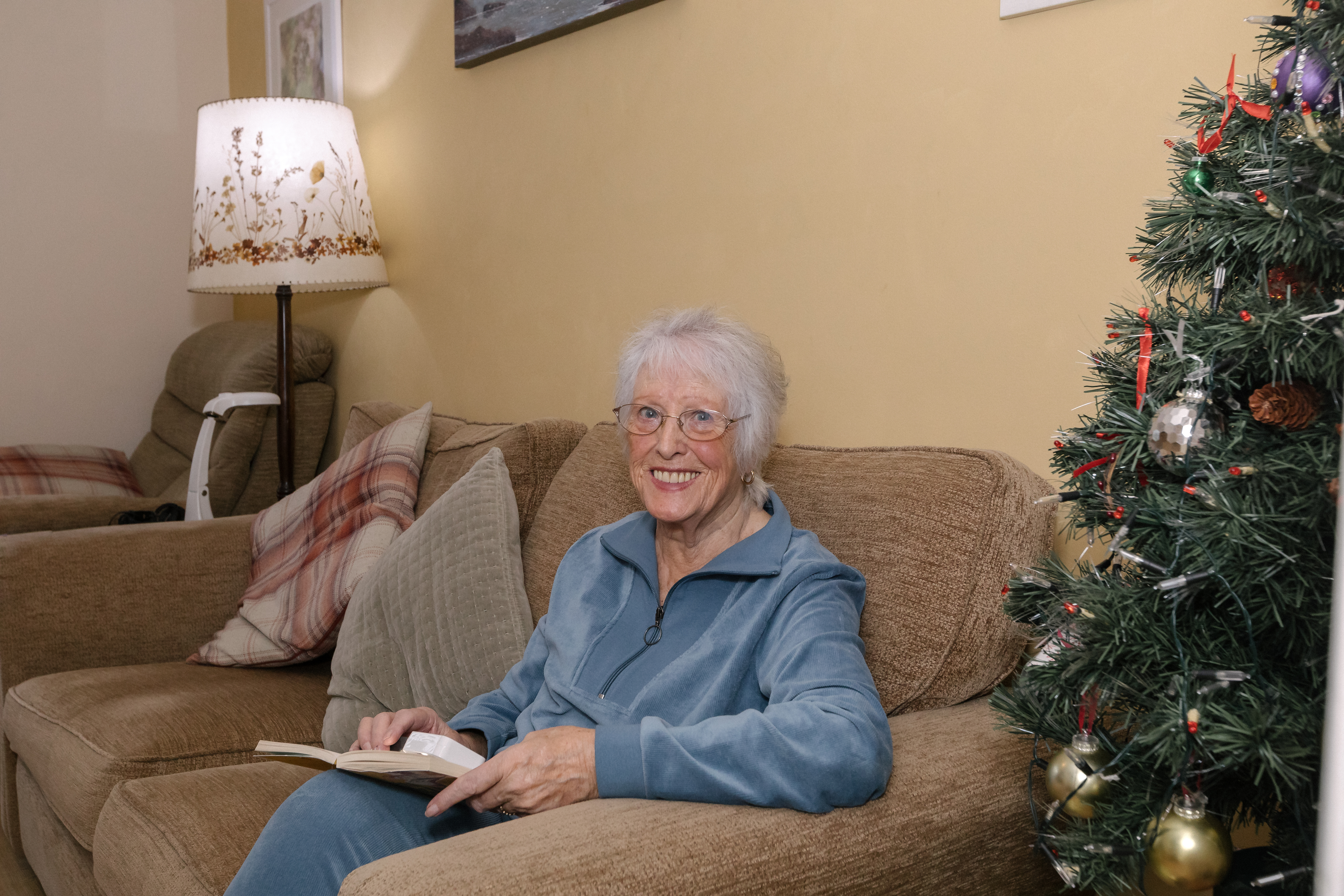Margaret Hughes smiling in living room, reading on sofa