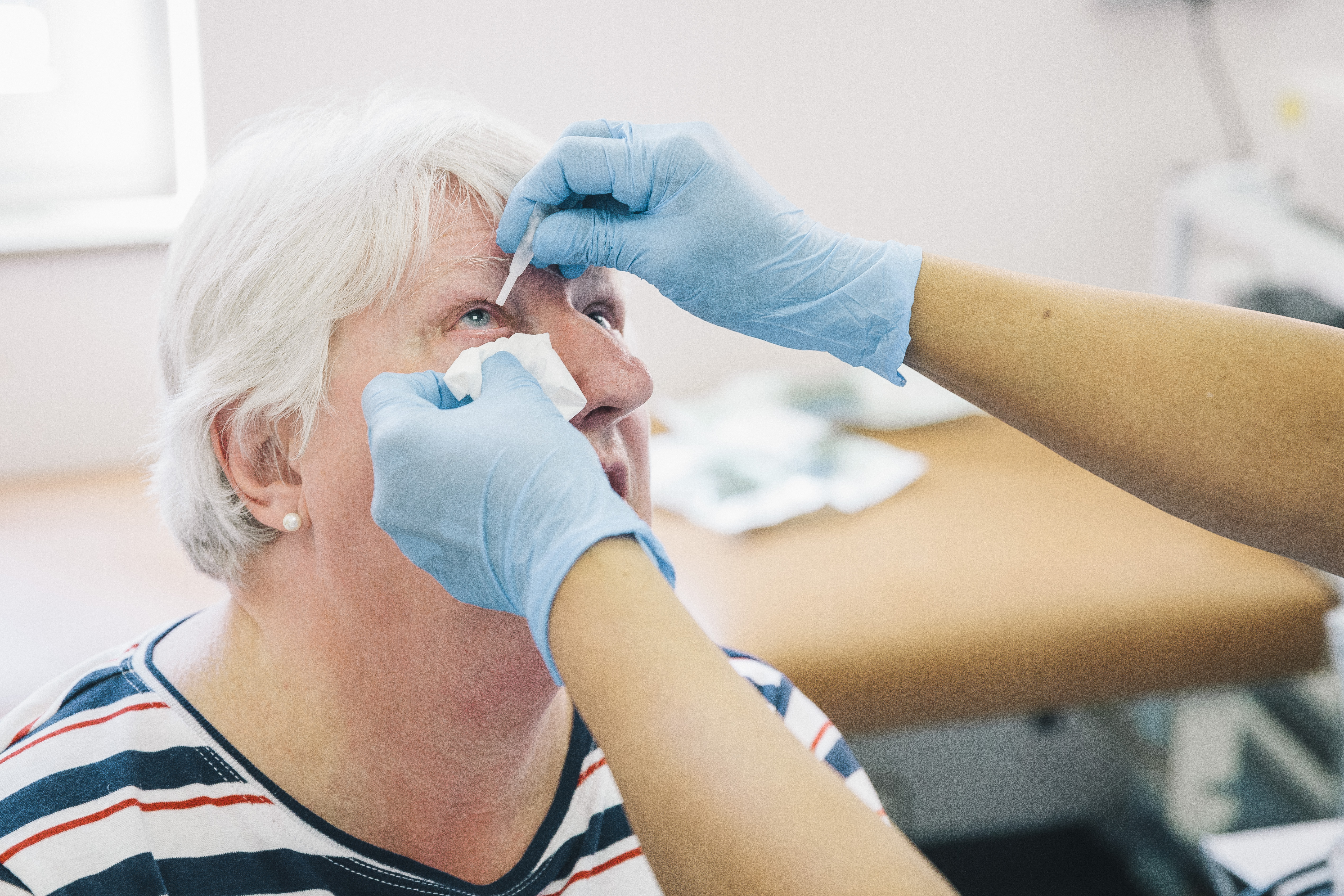 Eye drops being instilled into patient by professional with blue gloves.